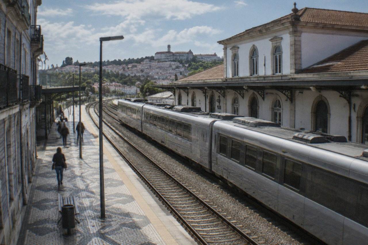 A railway platform in Coimbra with a train waiting beside the station building under a clear sky