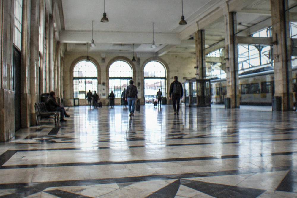 The interior of a Portuguese railway station with departure boards and passengers waiting with bags