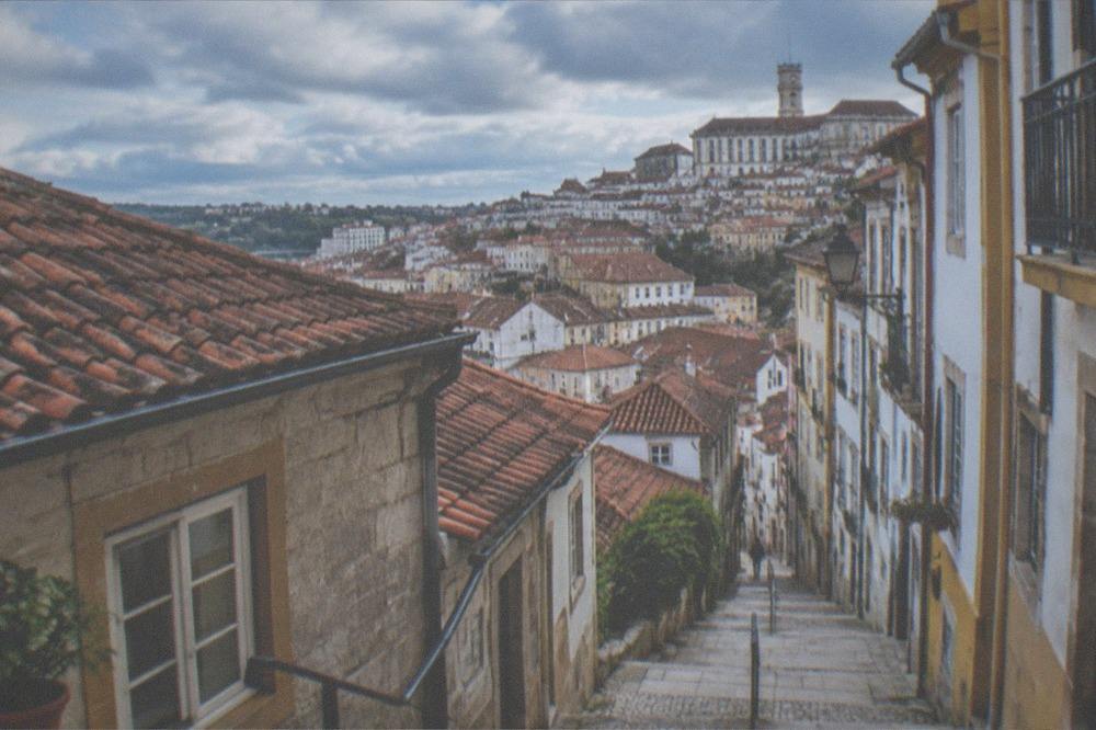 A steep narrow street in Coimbra's old town with stone buildings and a view over the city