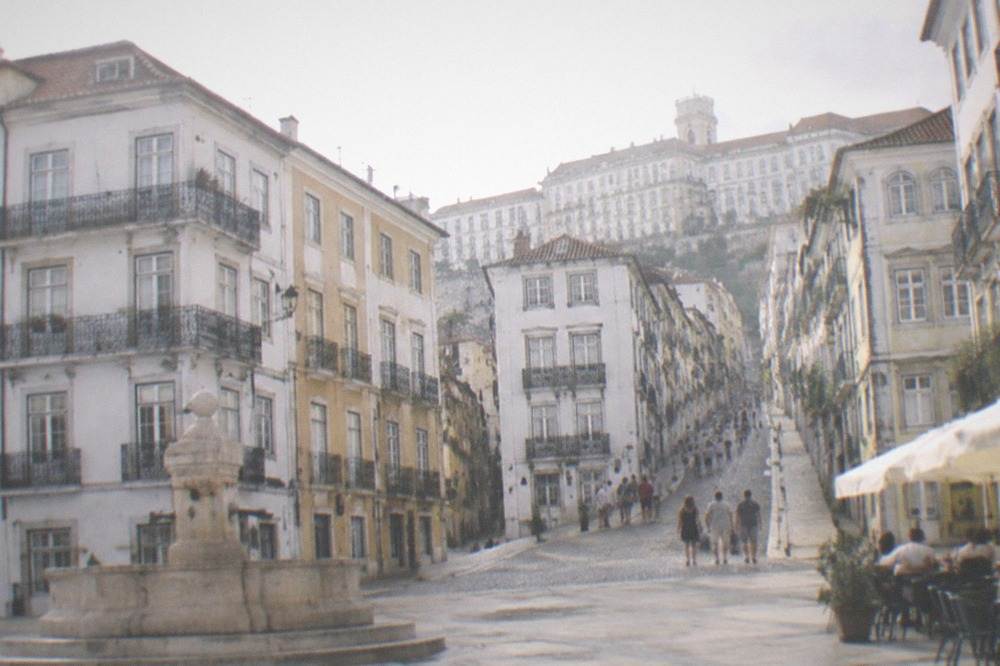 Visitors walking up a steep cobbled lane toward the university buildings in Coimbra's upper town