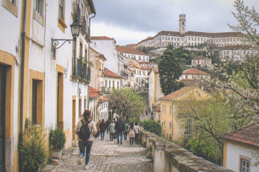 The hilltop university buildings of Coimbra seen from below with crowds in the streets