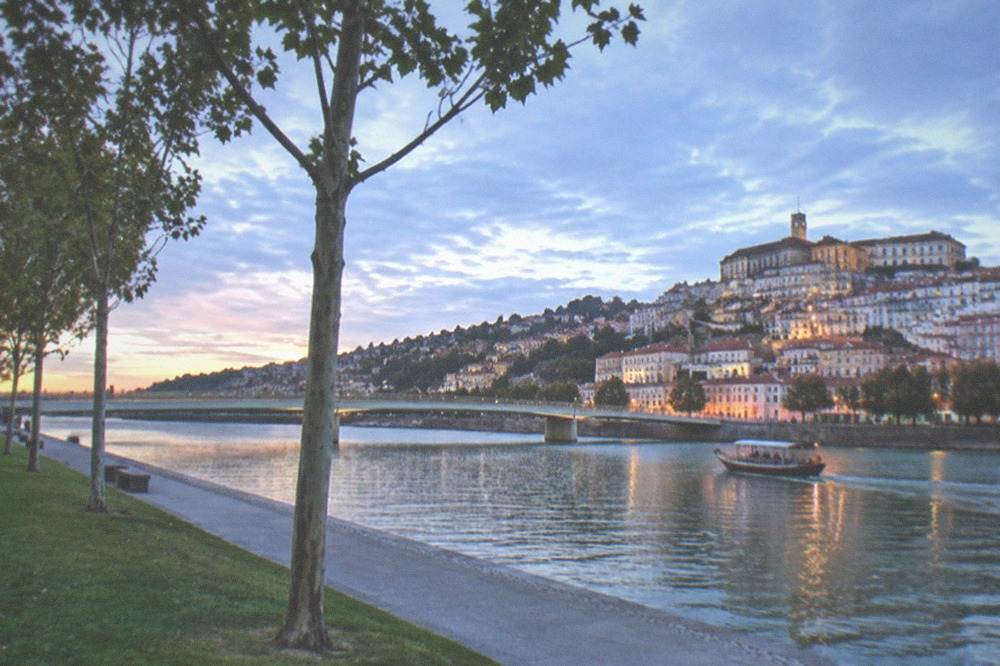A small boat on the River Mondego with the old town and university buildings on the far bank