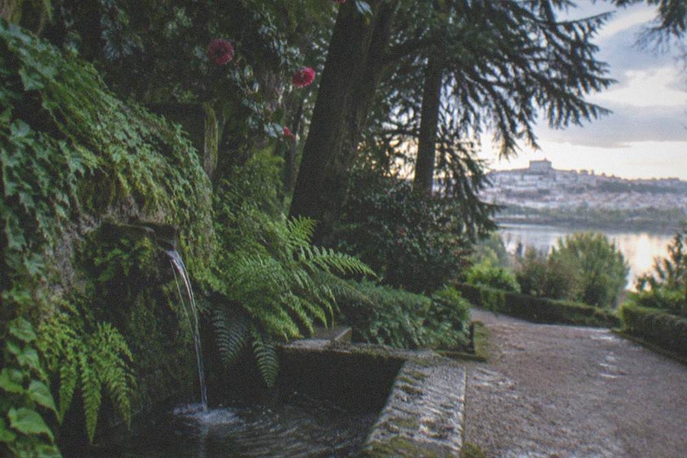 A hotel terrace at dusk with gardens sloping toward the River Mondego and city lights beyond