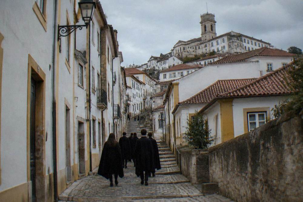 Students in dark capes walking together up a cobbled street in Coimbra