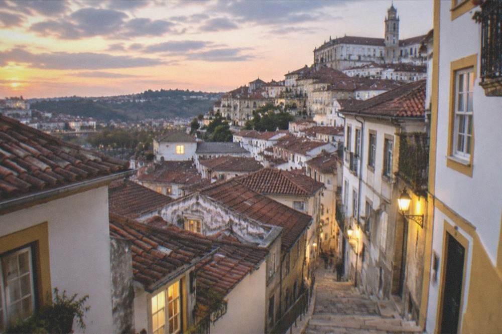 An evening view over the rooftops of Coimbra with warm lights in windows