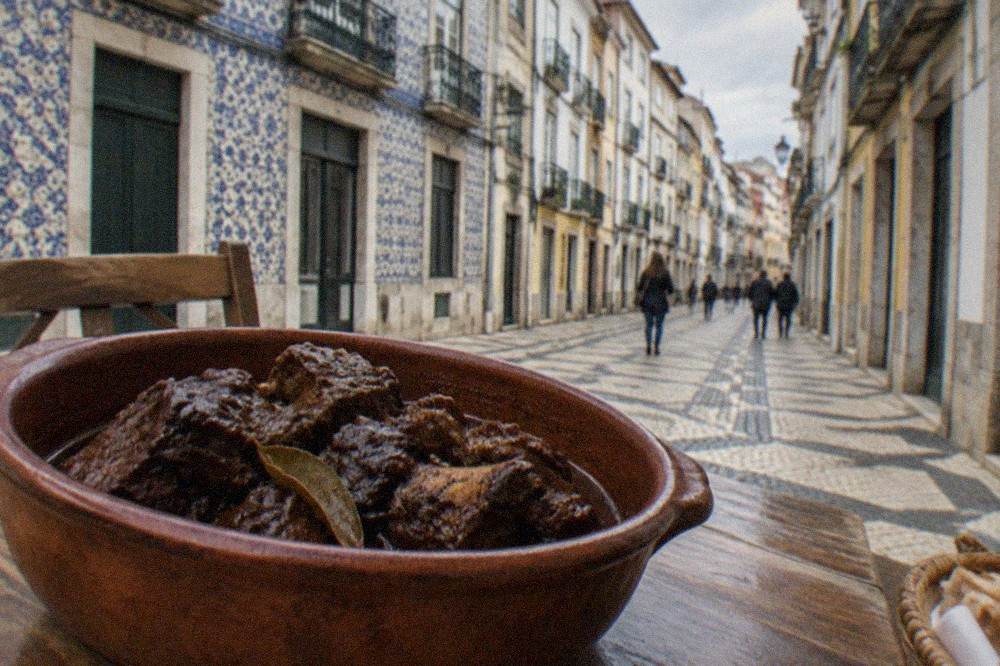 A clay pot of chanfana, dark braised goat meat in red wine sauce, on a rustic wooden table