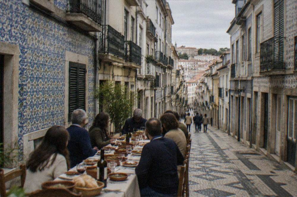 A long family lunch table set with clay dishes, bread and bottles of red wine