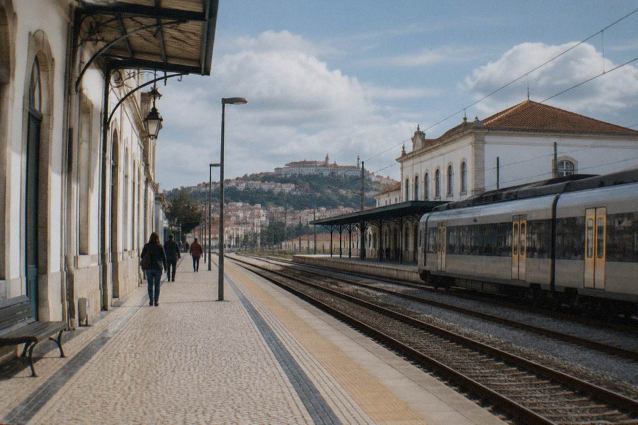 A railway platform in Coimbra, Portugal, with a train waiting beside the station building