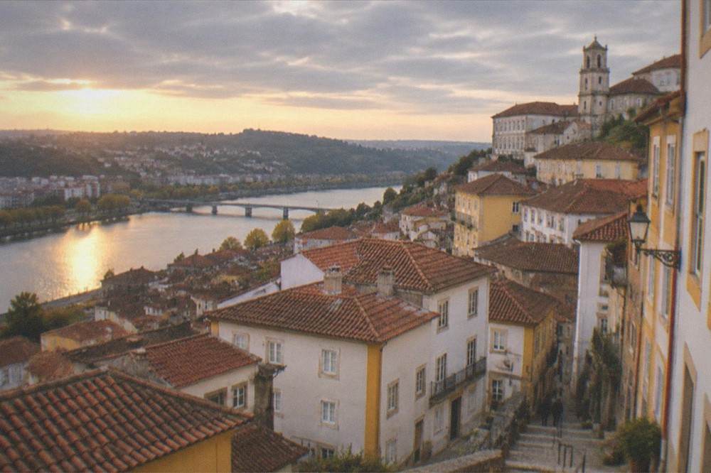 A view over Coimbra rooftops at golden hour with the river winding below the city.