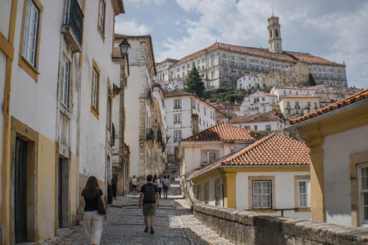 Visitors walking up a cobbled street toward the University of Coimbra on a sunny afternoon