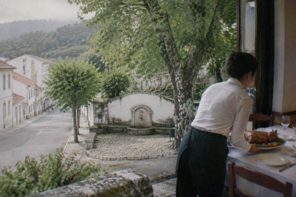 A server placing a plate of roast suckling pig on a restaurant table in Coimbra