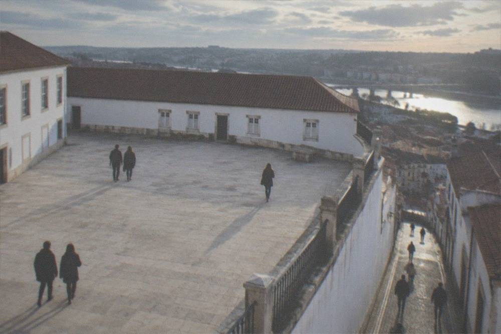 A cobbled street of college buildings running flat towards the river, with students walking along it