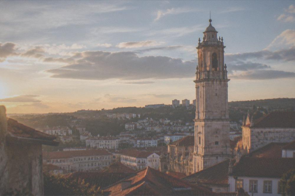 Warm evening light over the tiled roofs of Coimbra with the university tower rising above the city