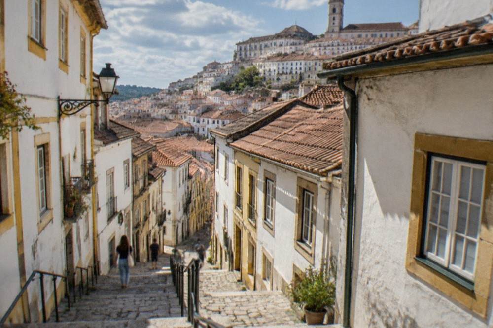 A sunny street in Coimbra's old town with sunlight on whitewashed walls and stone steps