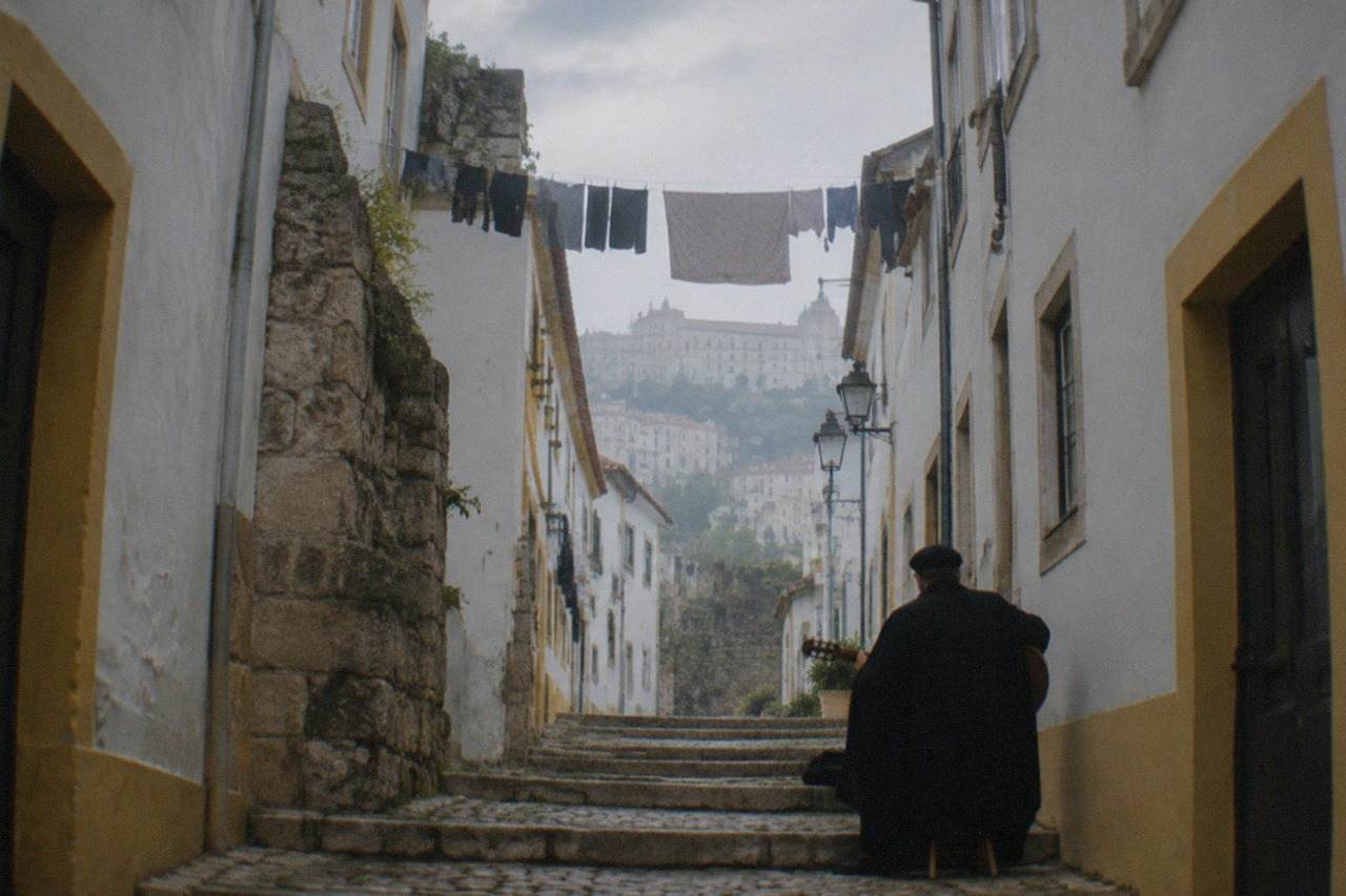 A guitarist and singer in dark academic capes performing fado in a dimly lit stone room in Coimbra