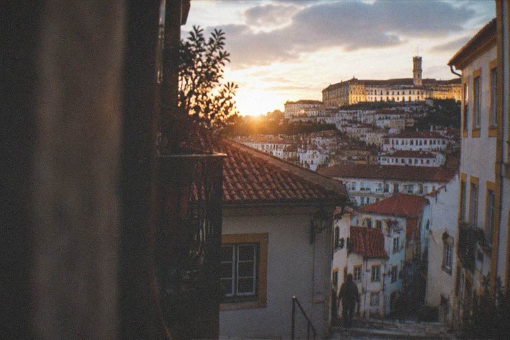 The lit facade of the old university above the dark rooftops of Coimbra at night