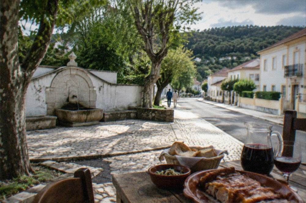 A rustic lunch table with roast pork, bread and a pitcher of red wine in a stone village house