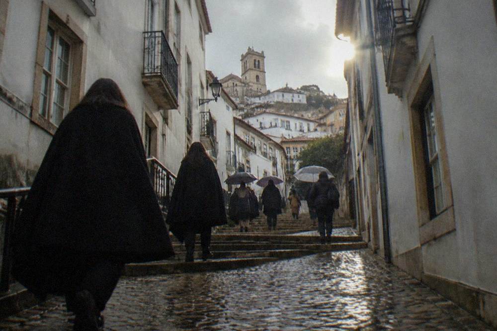Students in black capes walking up a narrow cobblestone lane in Coimbra's upper town
