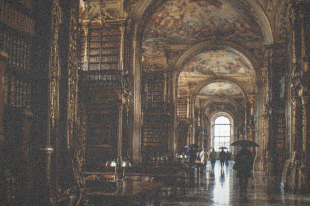 The baroque interior of the Joanina Library in Coimbra with tall gilded bookshelves and painted ceilings