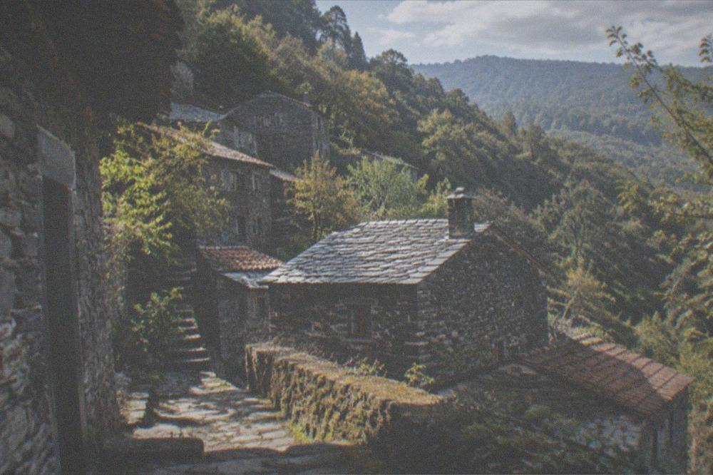 A stone schist village on a forested mountainside with slate-roofed houses.