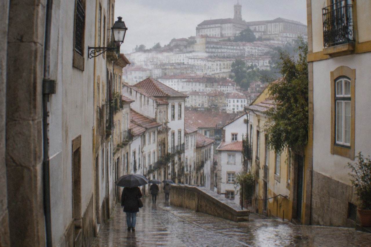 Wet cobblestone street in Coimbra's old town with rain-slicked stone buildings and umbrellas