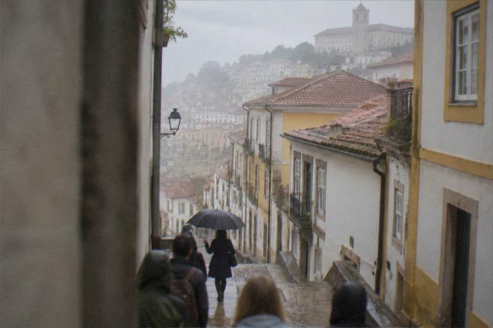 Tour guide with umbrella leading a small group of visitors through a rainy street in Coimbra