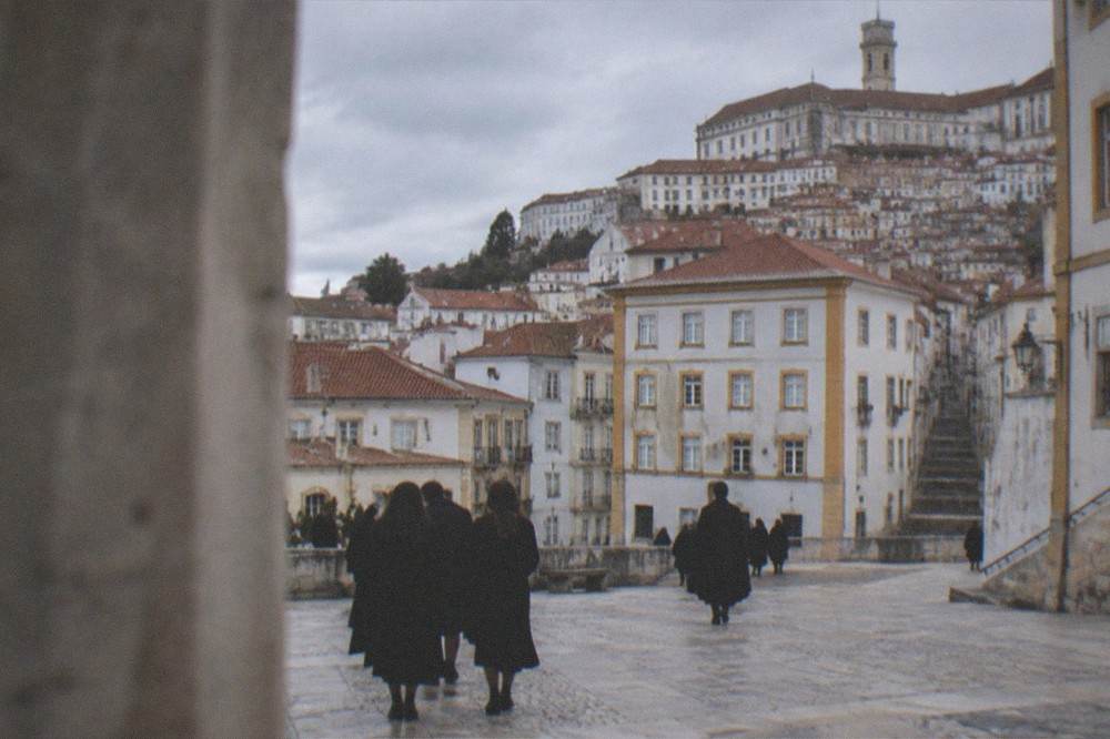 Students in black capes walking through a Coimbra square near the university